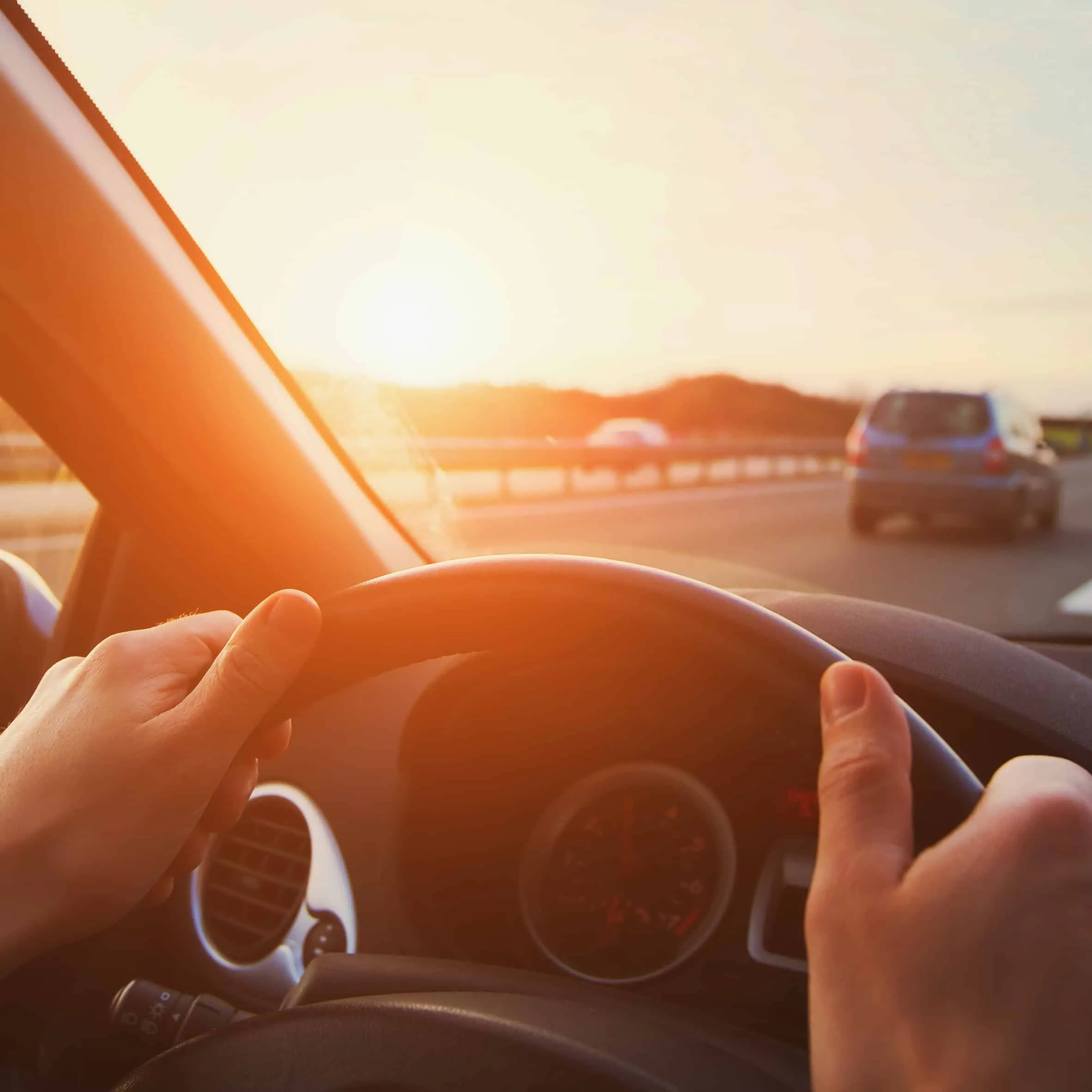Mains sur le volant d'une voiture roulant sur une autoroute au soleil