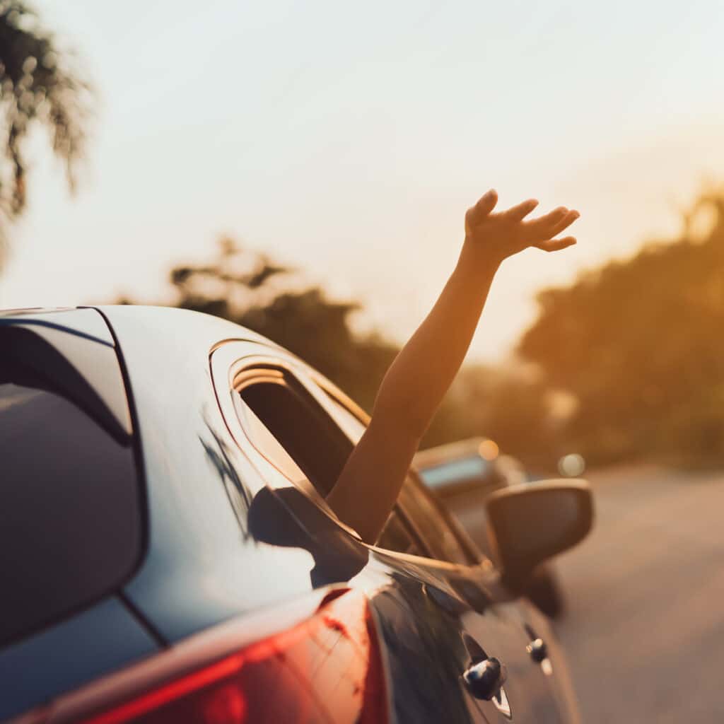 Bras en l'air sortant d'une voiture au soleil couchant Bras levé d'une personne sortant de la fenêtre d'une voiture roulant au coucher du soleil avec des reflets chauds.
